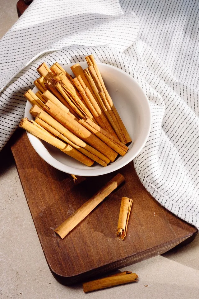 Cinnamon sticks in a white bowl on a wooden board.