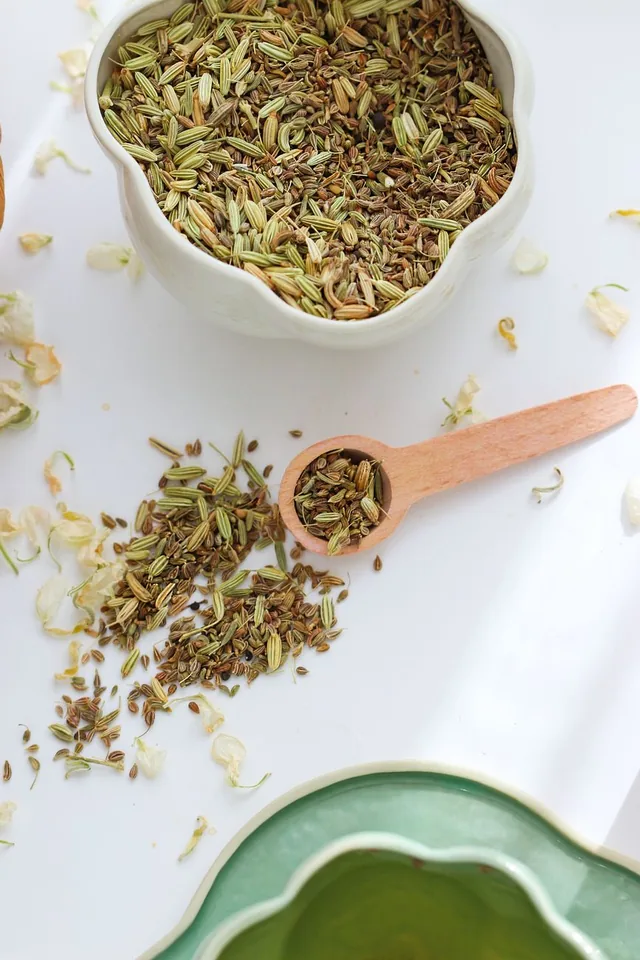 Fennel seeds in a bowl beside a wooden spoon.