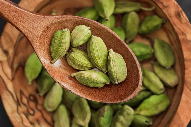 Green cardamom pods in a wooden spoon.