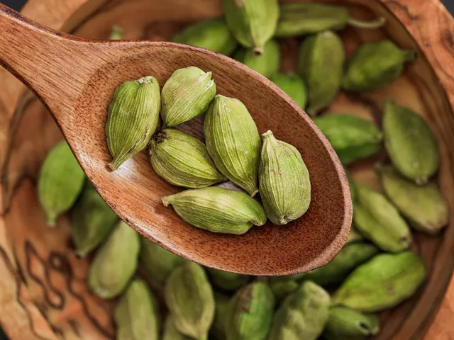 Green cardamom pods in a wooden spoon.