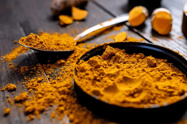 Turmeric powder and sliced fresh turmeric on a dark wooden surface.