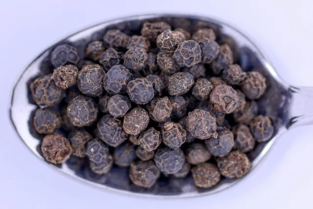 Whole black peppercorns in a metal spoon.