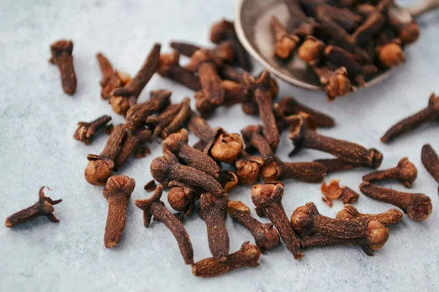 Whole dried cloves scattered beside a spoon.
