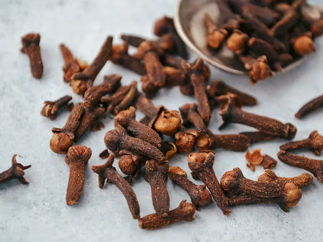 Whole dried cloves scattered beside a spoon.